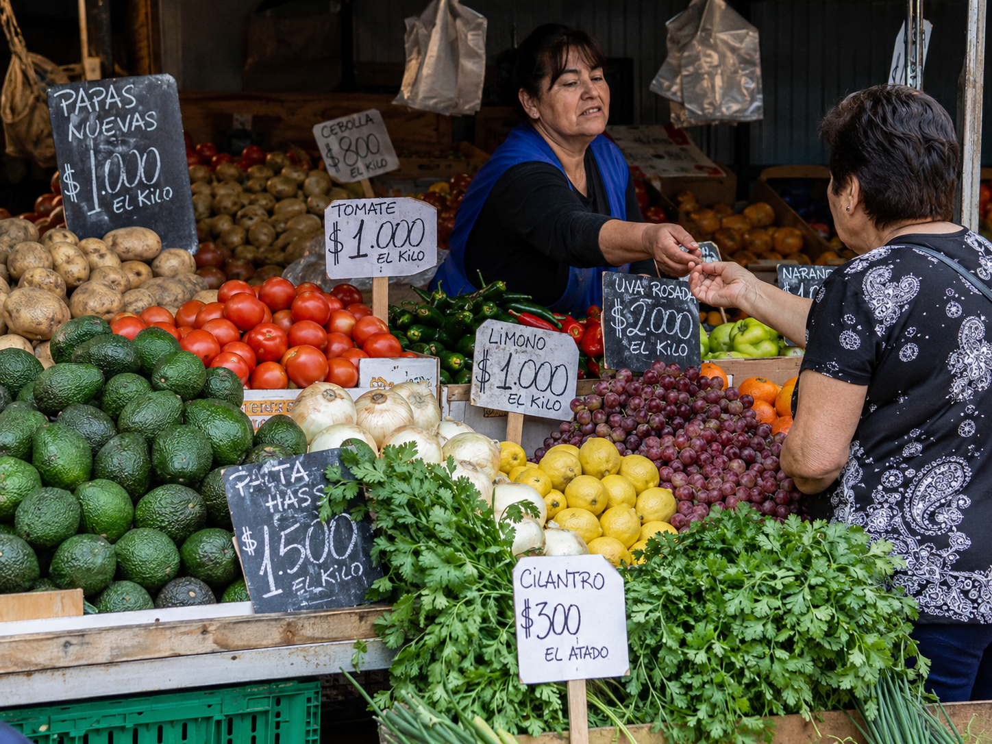 Vendedora de feria libre entregando cambio frente a frutas y verduras frescas.