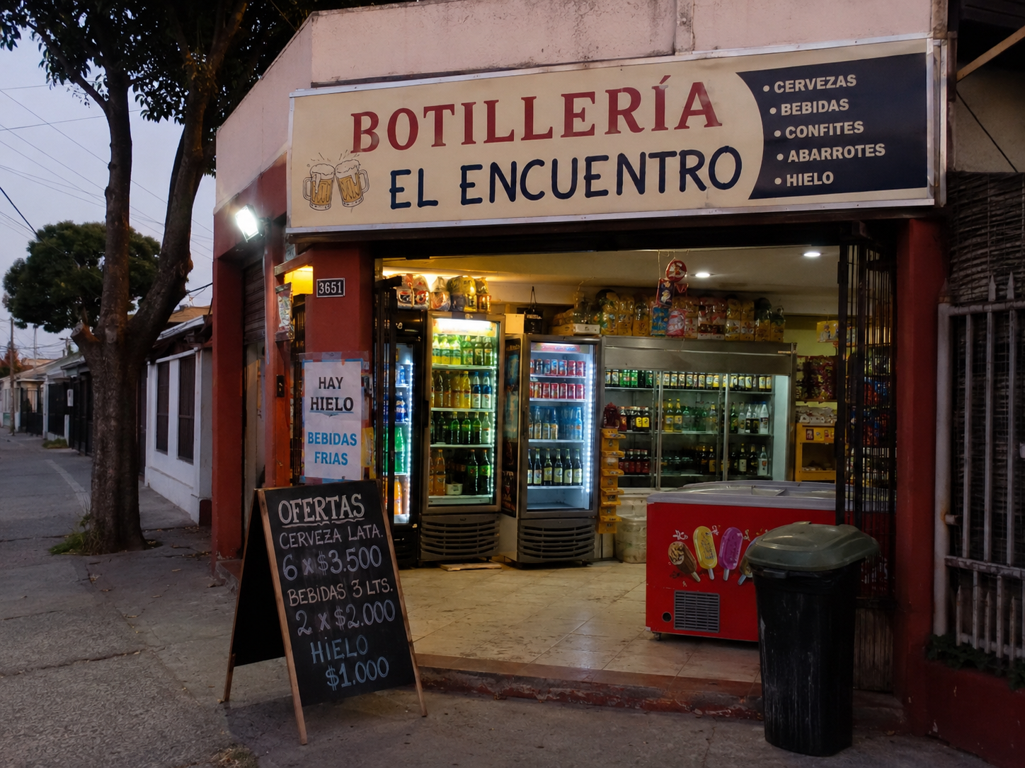 Botillería El Encuentro iluminada al atardecer con vitrinas de bebidas y cartel de ofertas.